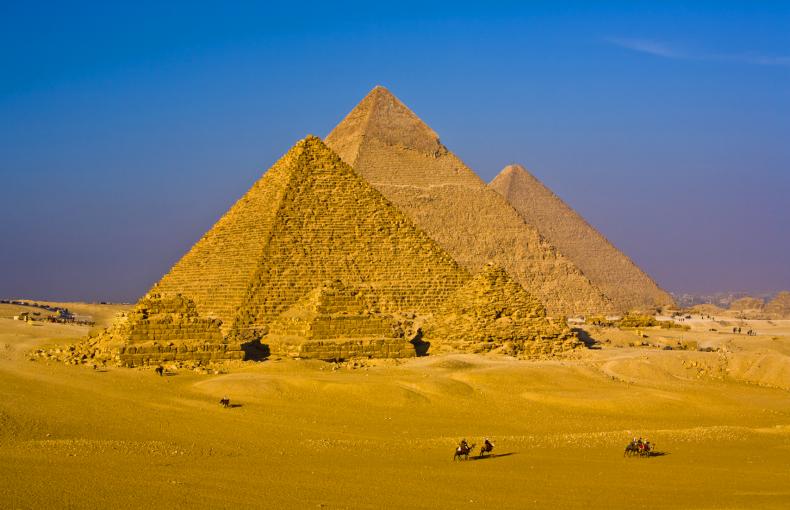 Two people riding cameras past Egyptian Pyramids