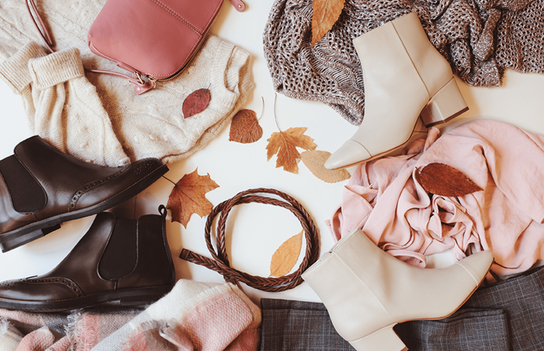 A collection of earth tone leather shoes, sweaters, and handbags with fall leaves sprinkled across the apparel.