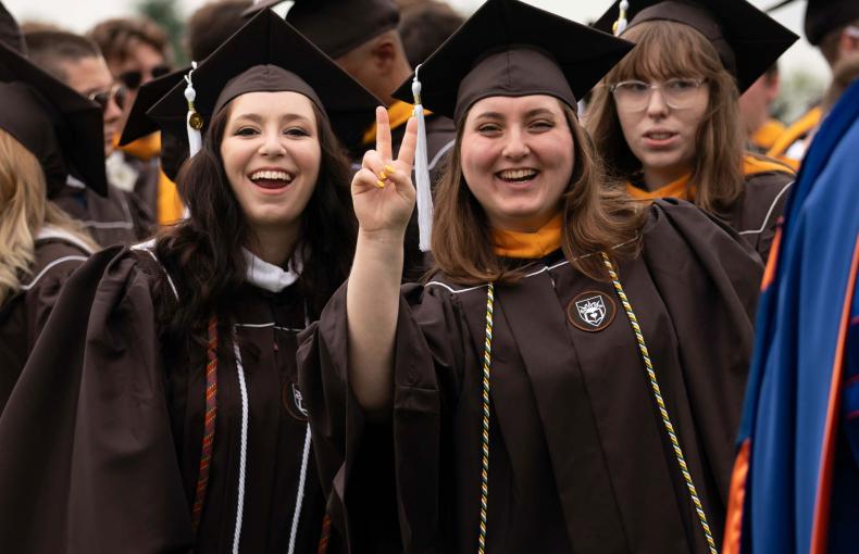 Two female graduates smiling and dressed in their commencement regalia