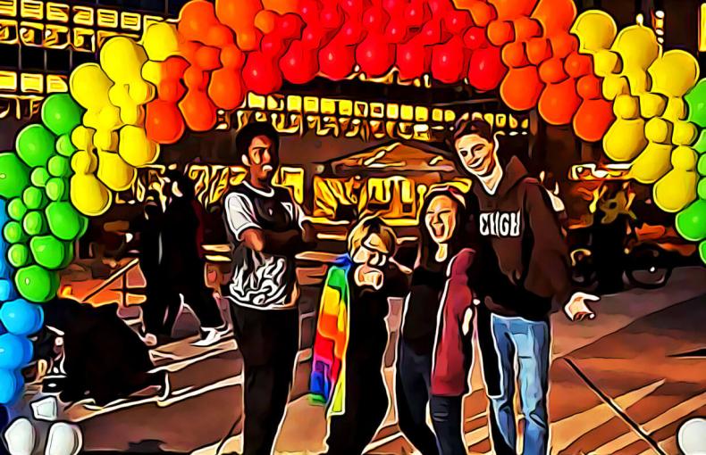 Four students standing under a rainbow balloon arch