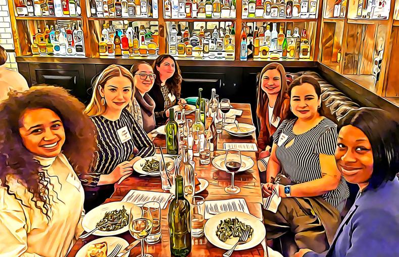 Women sitting around a table for dinner and smiling at the camera