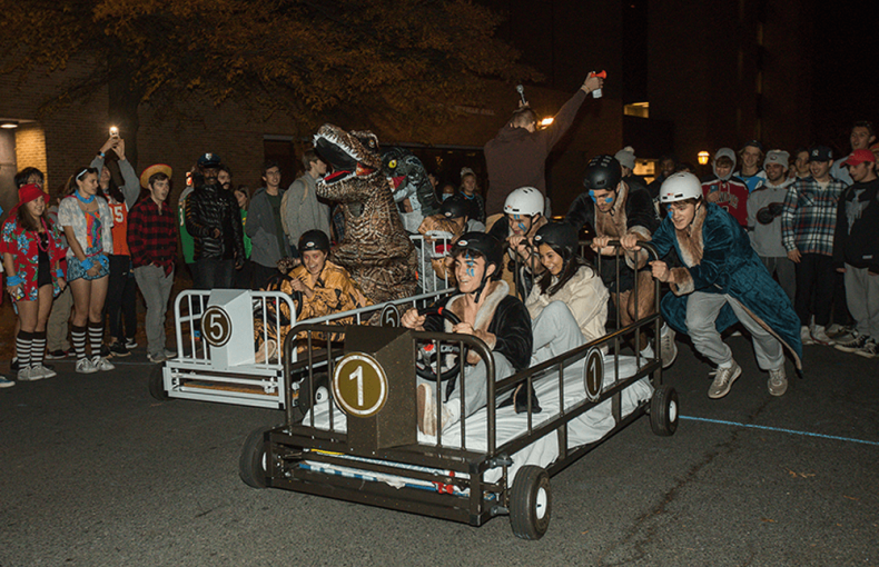Lehigh students dressed in costumes race bed-shaped cars down a road.