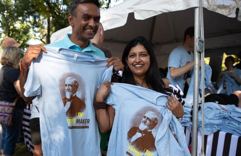 Two people smile for the camera while holding up two light blue t-shirts with an image Asa Packer on the front.