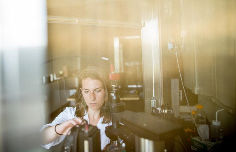 A researcher in a white lab coat adjusts a piece of scientific equipment in a laboratory setting.
