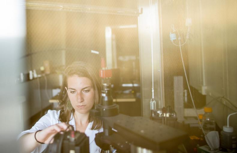 A researcher in a white lab coat adjusts a piece of scientific equipment in a laboratory setting.