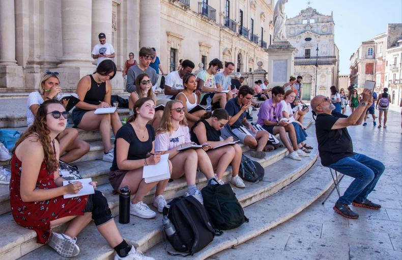 Students gathered together, seated on steps, with their notebooks in their laps