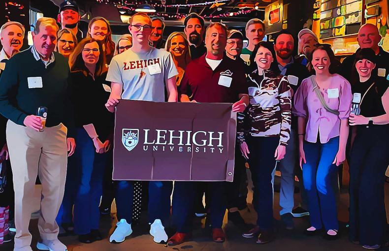 People gather for a group photo while they proudly hold a Lehigh Flag