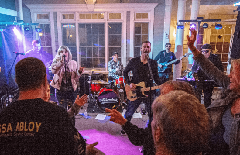 Live performance by the band The Weekenders on a lit porch stage for an energetic, dancing crowd at night.