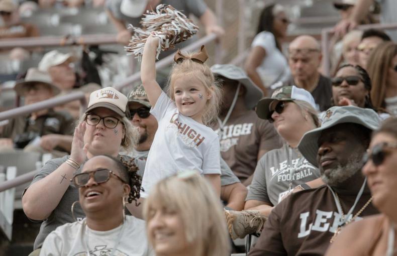A young child raises their pom-pom in the air while standing in the bleachers.