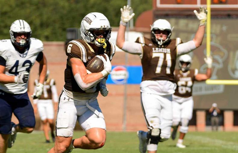 Luke Yoder carries the football downfield while a teammate celebrates behind him during a Lehigh University game.