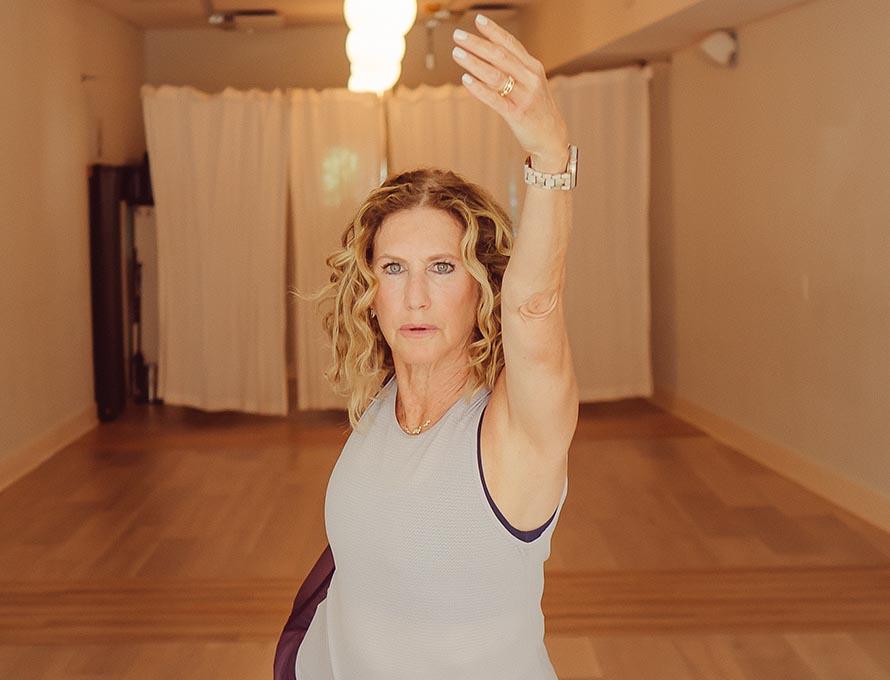 Kyle Greenberg '85 in a yoga studio raises her arm and holds her foot in a yoga pose