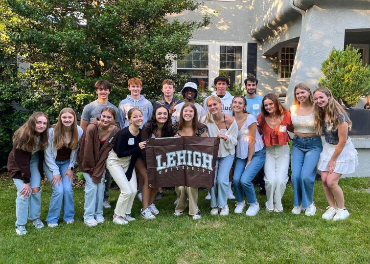 Smiling incoming students grouping together for a photo and proudly holding a brown Lehigh banner.