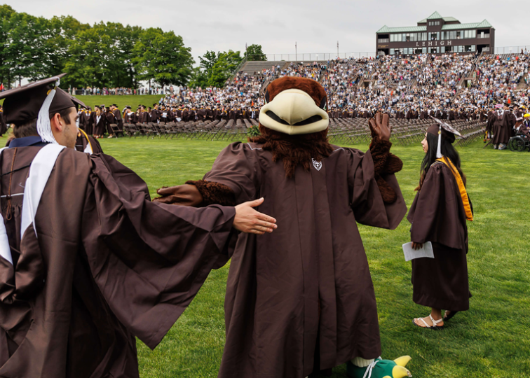 Lehigh University Mascot, Clutch, dressed in graduation regalia and high-fiving a Lehigh graduate during a commencement ceremony at Goodman Stadium.