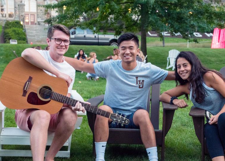 Three Lehigh University students sitting in Adirondacks chairs on the Clayton University Center lawn.