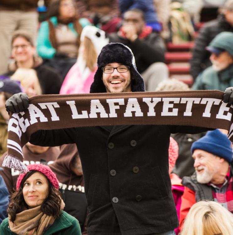 Man holds brown Beat Lafayette scarf in the crowd of a football game