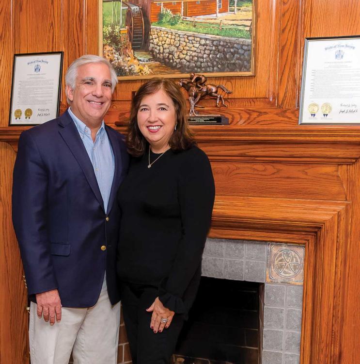 Sharon and James Maida standing and smiling together before their fireplace. 