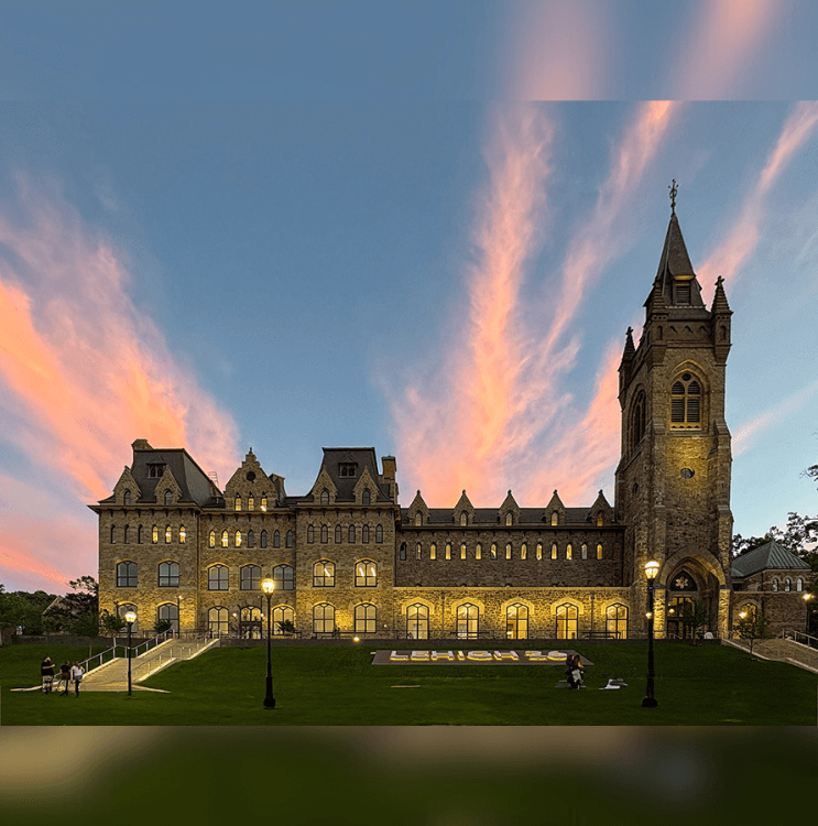 Stone university building lit up in front of the evening sky.