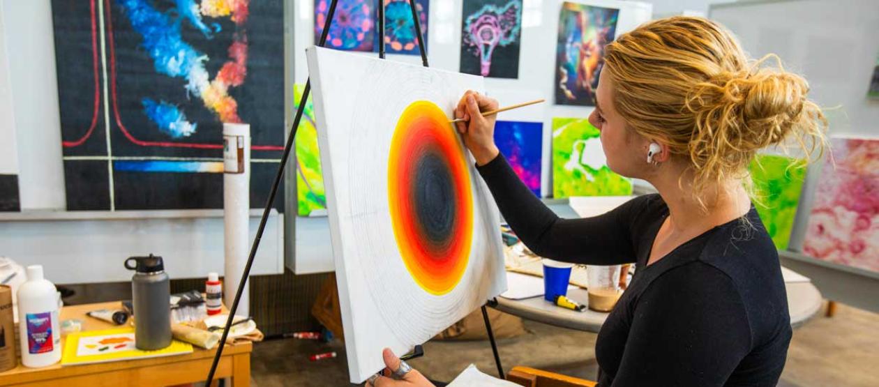 A young woman painting on a canvas in a classroom