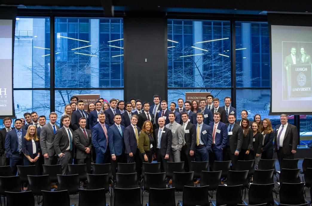 Students and alumni gather for a large group photo before floor to ceiling windows