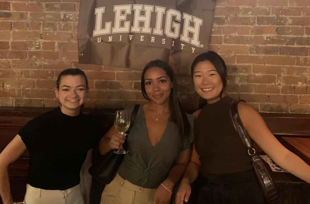 Three women posing under a Lehigh flag at 2022 NYC Happy Hour