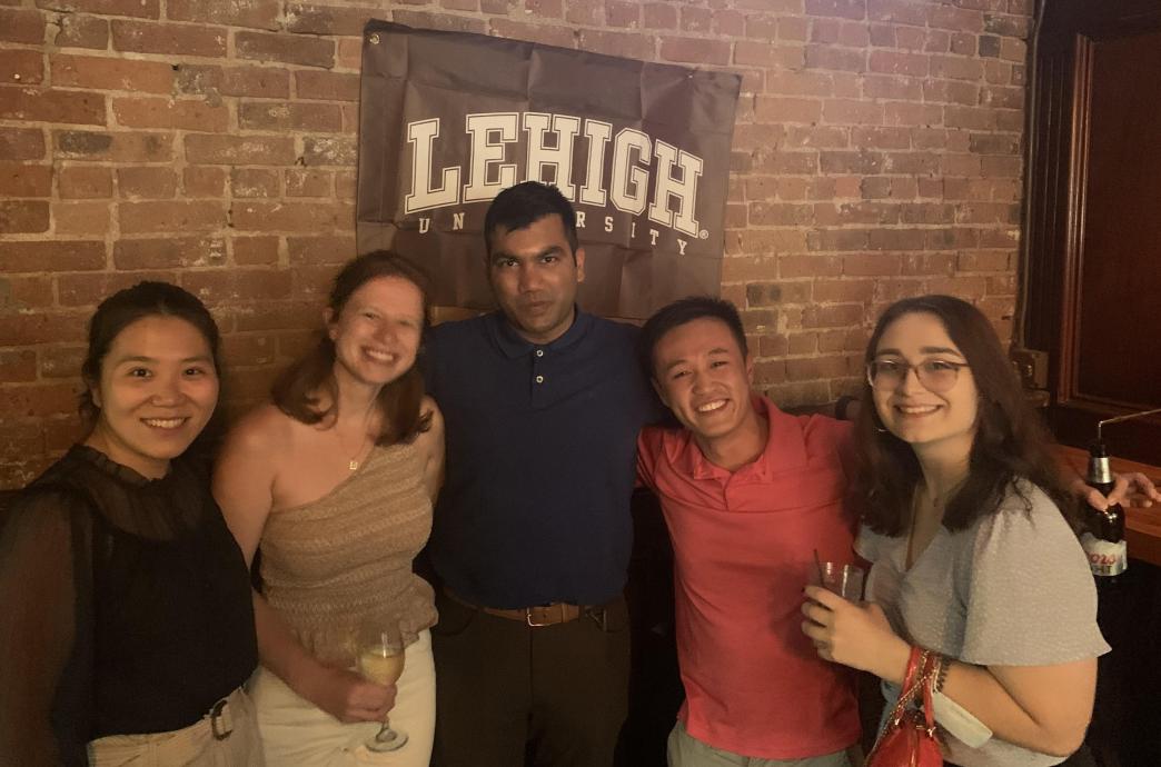 a group posing under a Lehigh flag at the Summer 2022 NYC Happy Hour