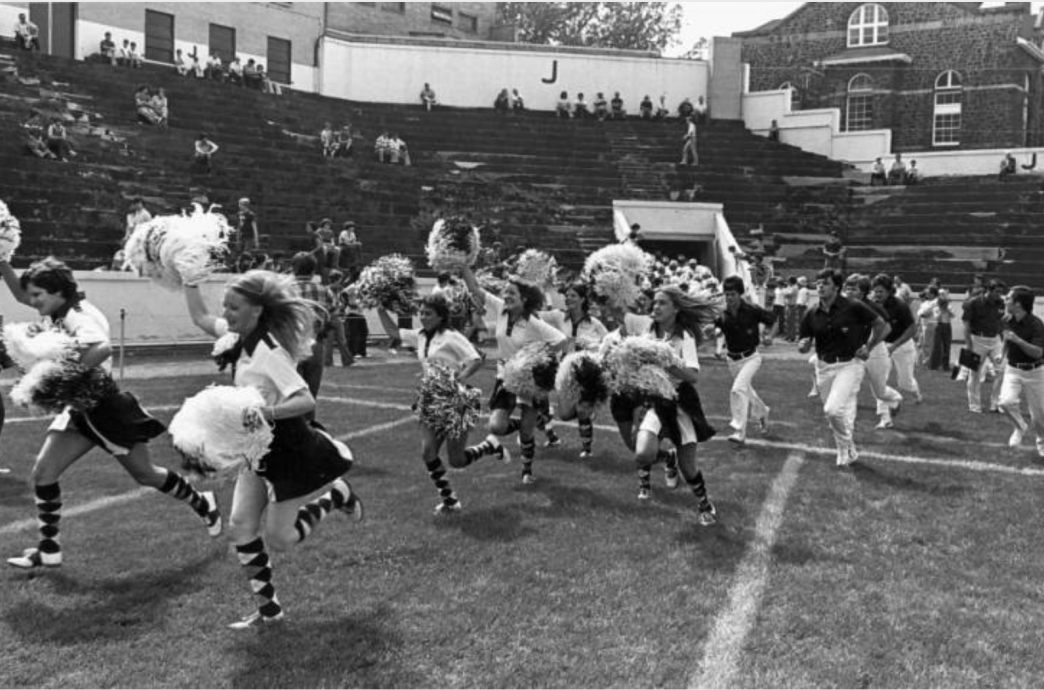 Cheerleaders charging onto the field with pompoms raised
