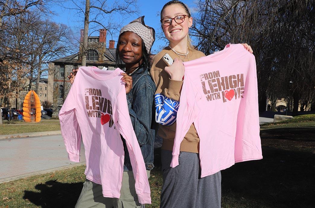 Two students stand back to back and hold shirts