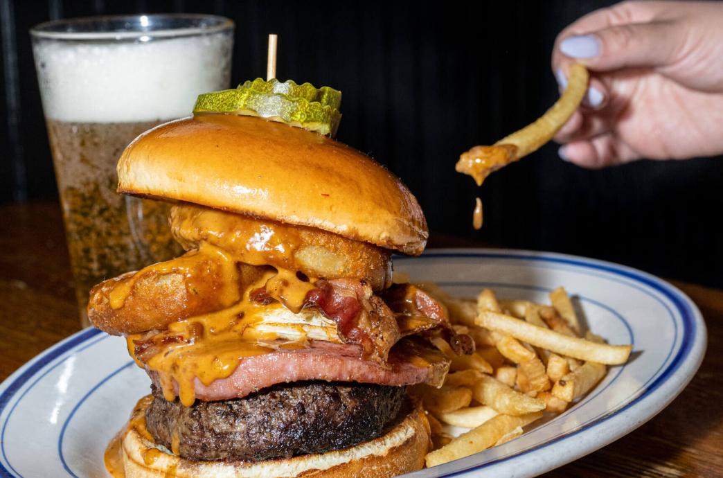 A stacked burger resting on a plate surrounded by crispy french fries