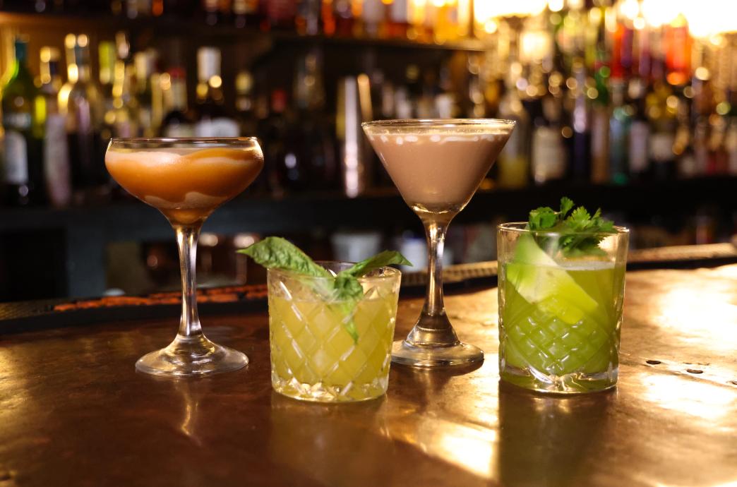 Four cocktails sit on the bar top topped with various garnishes 