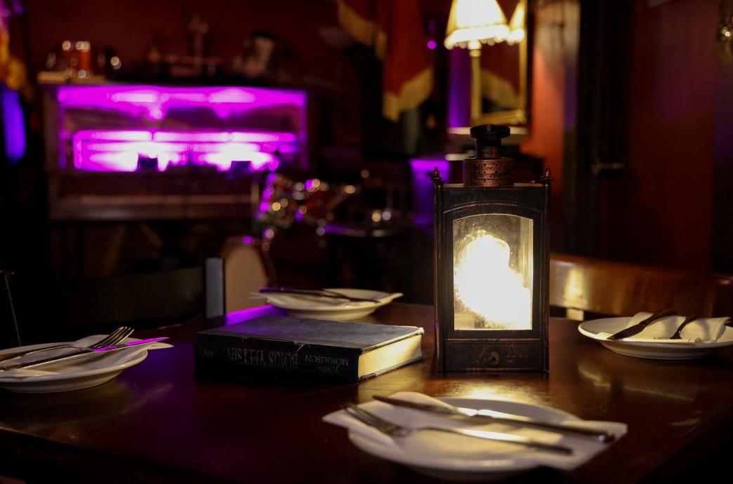 A table topped with place settings, a small lantern, and a vintage hardback book in a dimly lit room.