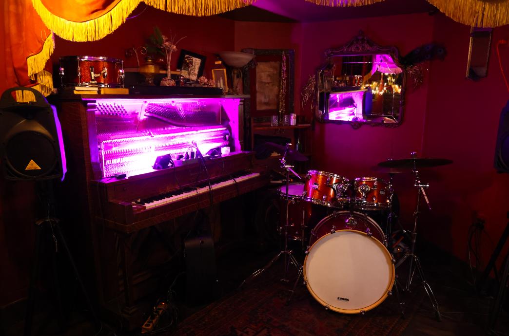 A piano and drum set are accented with purple florescent lights