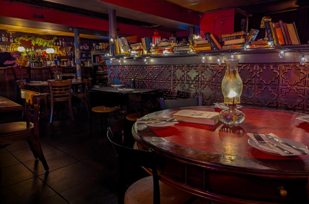 A full view of the room with set dining tables topped with lanterns and oil lamps and the bar in the background