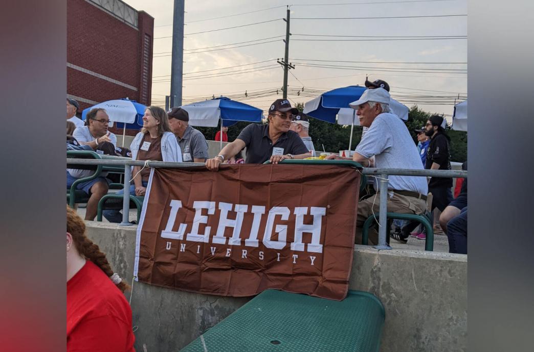 Two men chatting at a picnic table behind a Lehigh University banner