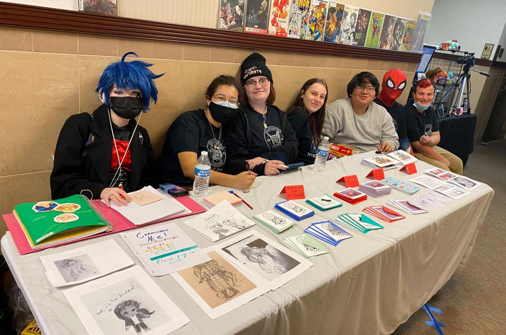 Students sitting behind a table showing their artworks at a Lehigh Valley Comic Con event