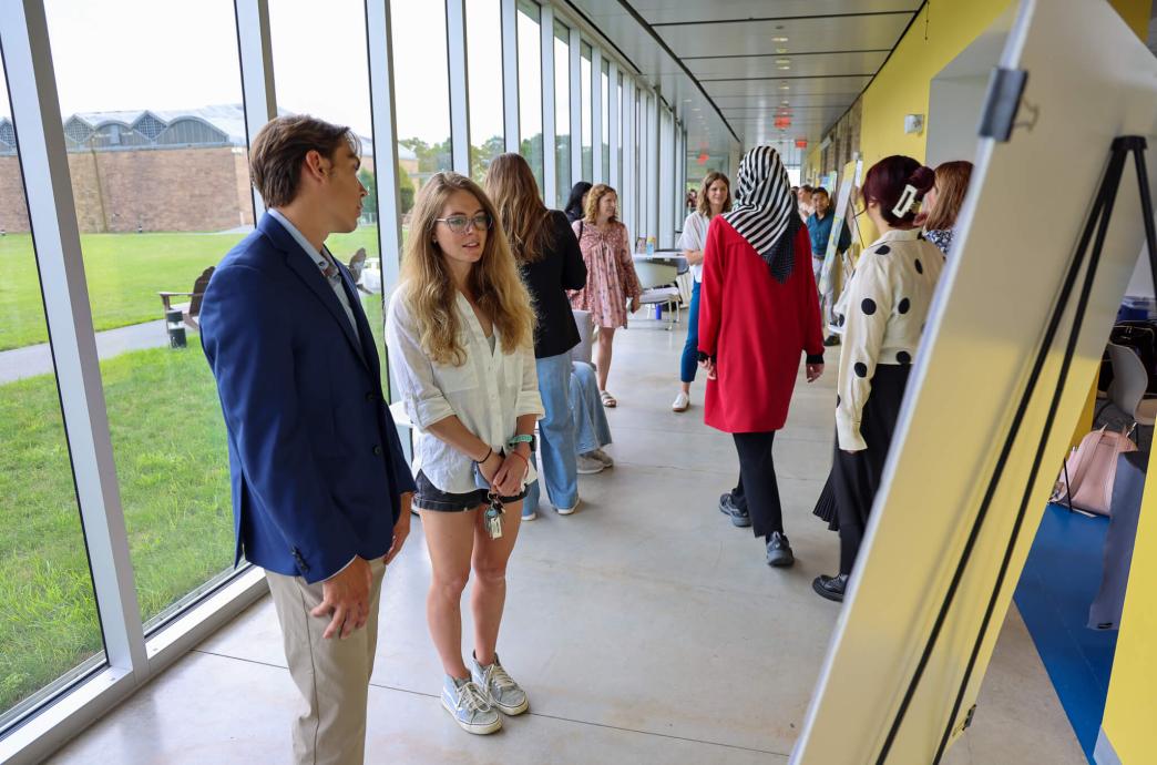 Will Filipovits standing near a window talking about his project with Haley Griner