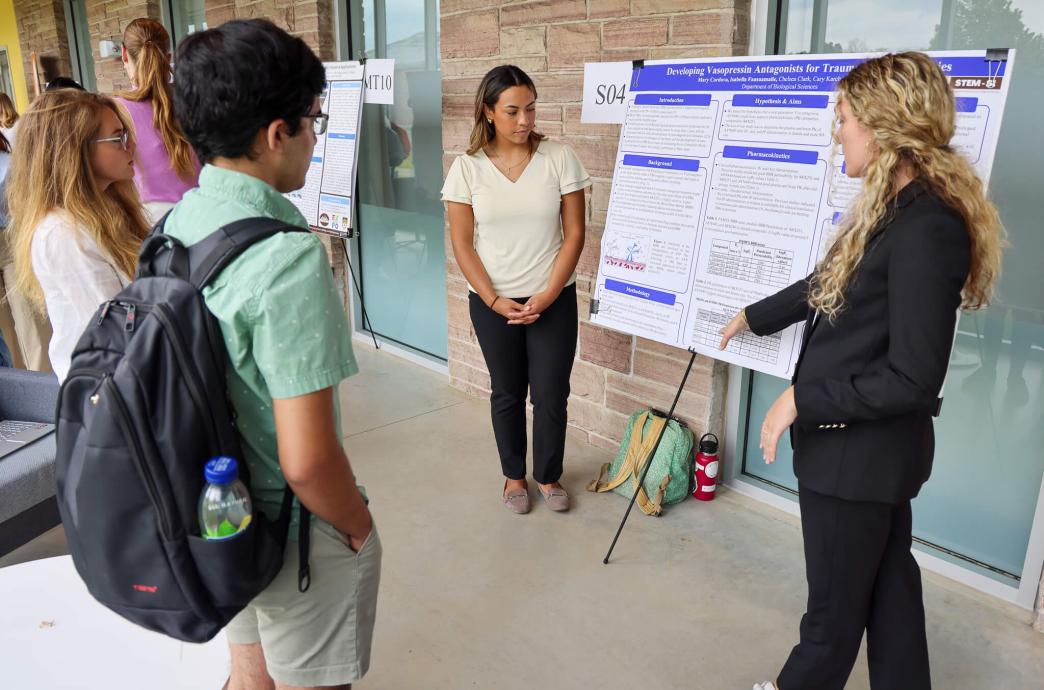 Isabella Faasaumalie and Mary-Evelina Cordova gesturing at their poster while others look on