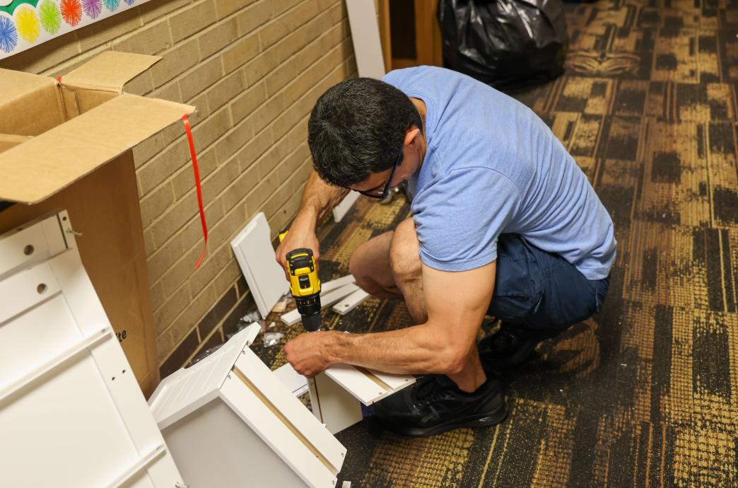 A dad building a shelf in the hallway of the dorm