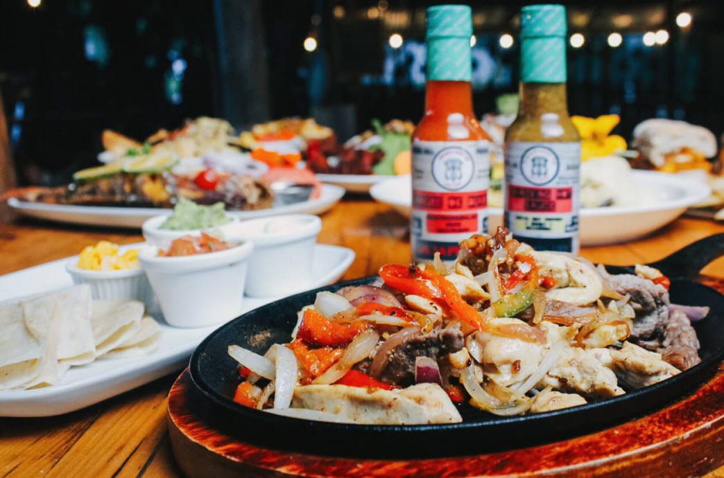 A loaded plate of Fajitas accompanied by a variety of hot sauces
