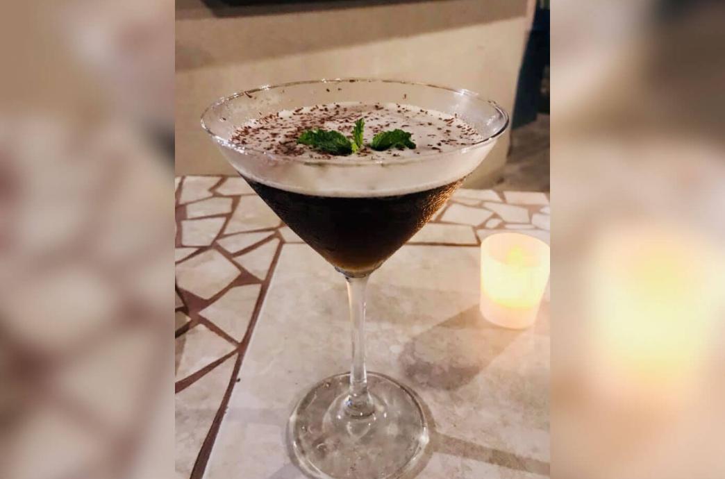 A dark martini next to a candle