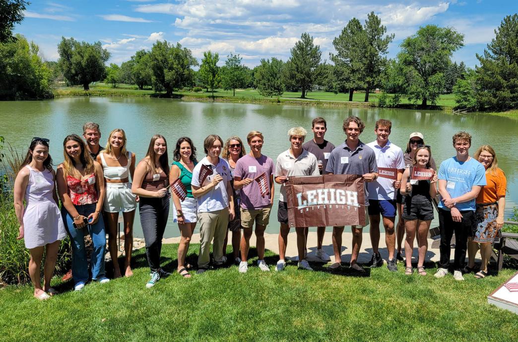 Incoming students posing with a brown Lehigh University flag in front of a lake