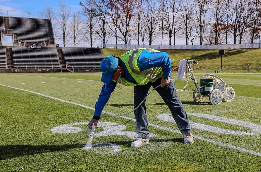 Juan Montero paints the white yard marker on the football field of Goodman Stadium.