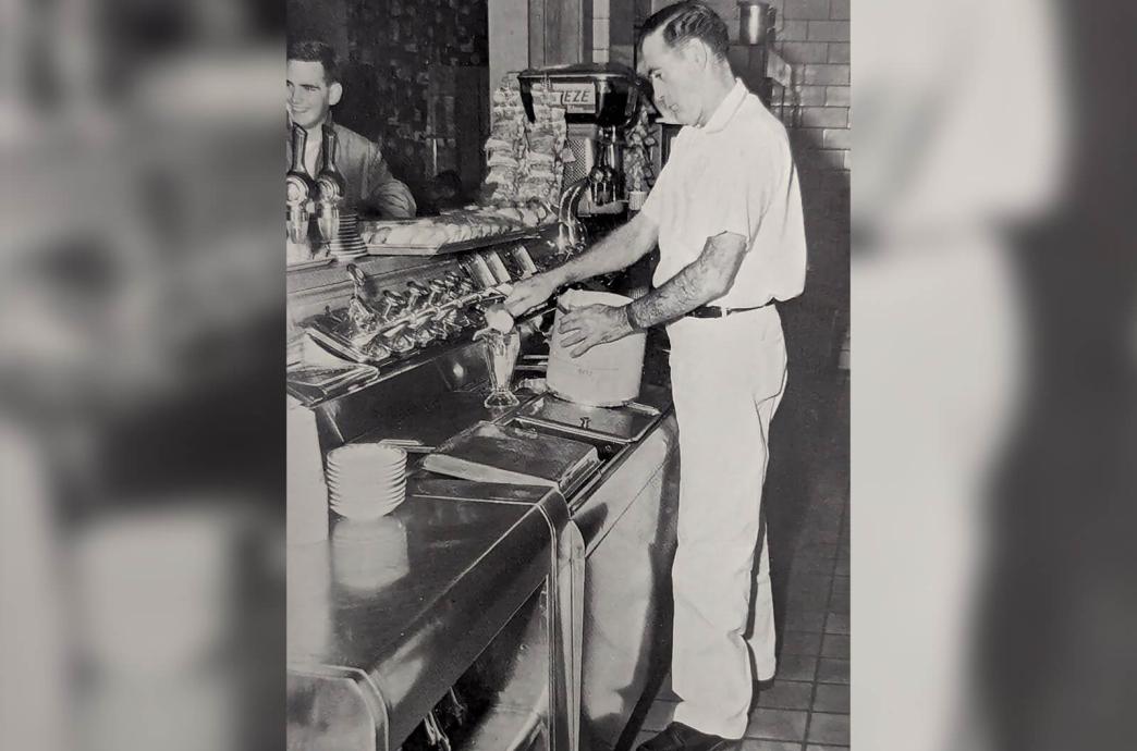 Black and white photo from the 1963 yearbook shows a man behind a counter scooping ice cream into a glass dish with happy students waiting for their treat.