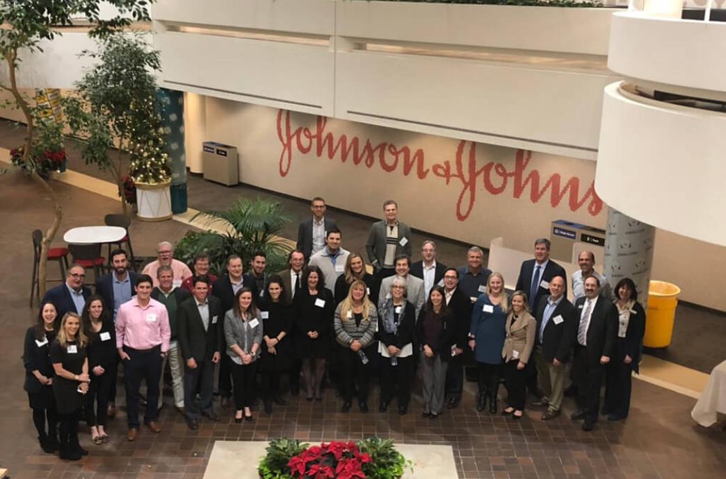 A large group of alumni pose in front of a Johnson & Johnson mural.