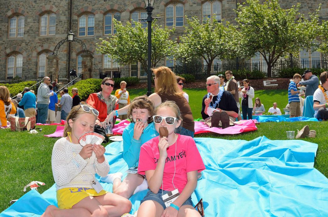 Kids sit on a blanket on the lawn at Reunion 2014 eating ice cream.