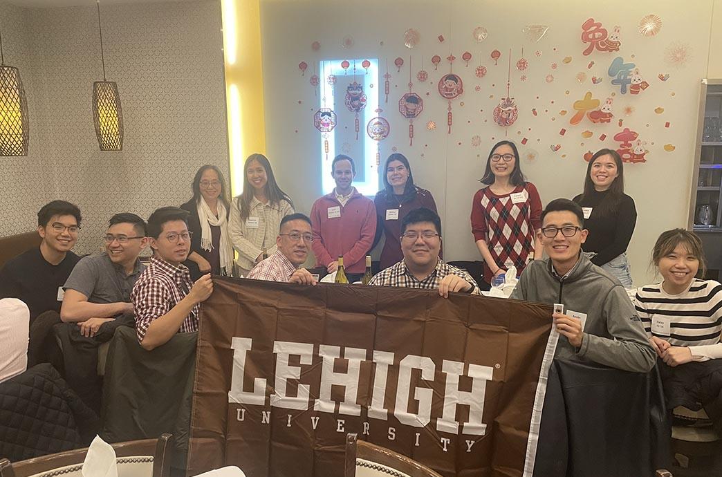 LAAN members hold a Lehigh banner at their event table with beautiful red decorations on the walls