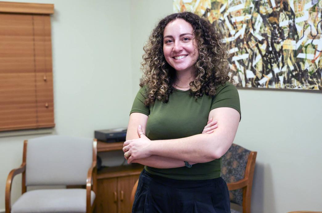 Jessica Safi stands with her arms crossed in front of her, smiling at the camera with an arm chair and painting behind her.