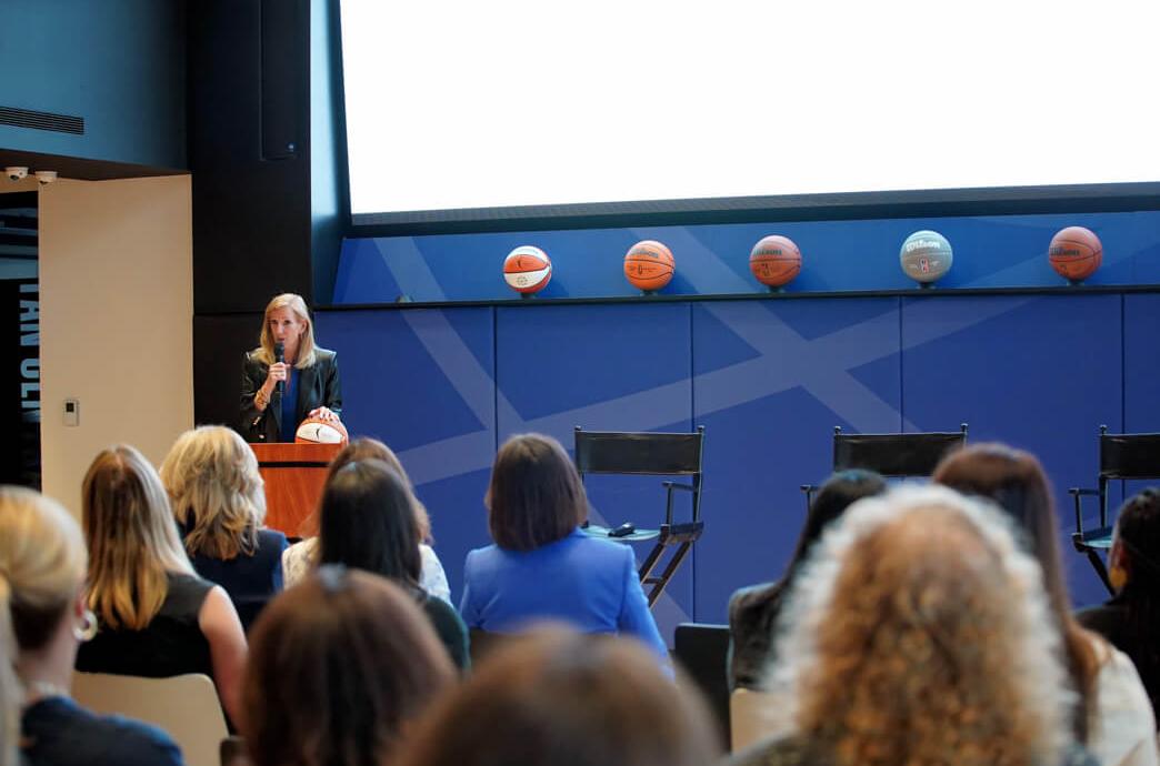 Cathy Engelbert stands at a podium and speaks to a room of Lehigh event attendees in WNBA HQ.