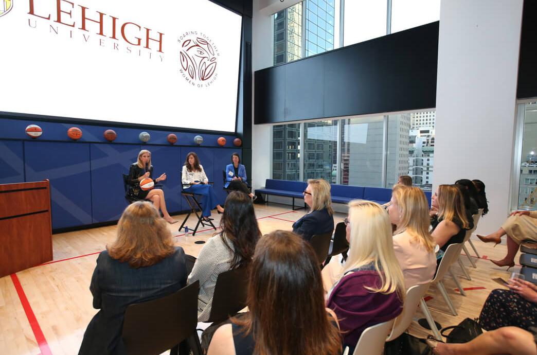 Cathy Engelbert and panelists talk at the front of a Lehigh event hosted at WNBA HQ as attendees look on.