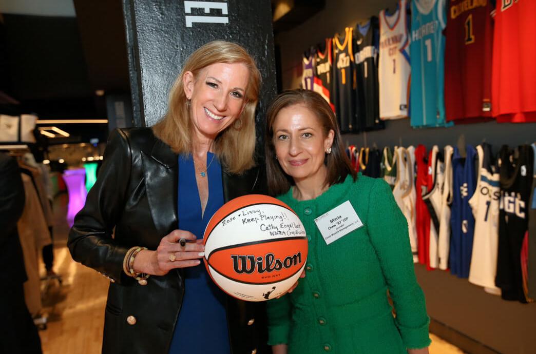 Cathy Engelbert poses with an alumna after autographing a basketball she is holding with a Sharpie marker.