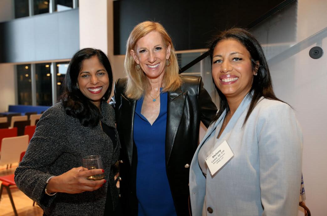 Cathy Engelbert, wearing a royal blue blouse under a black leather jacket, poses with two alumnae